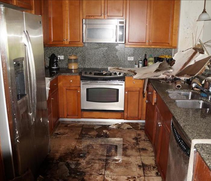 Kitchen with water damage on the floor and messy cabinetry.